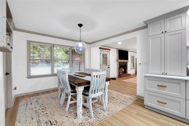 dining space with baseboards, a warm lit fireplace, crown molding, and light wood-type flooring