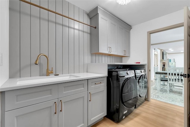 clothes washing area with cabinet space, independent washer and dryer, light wood-style flooring, and a sink