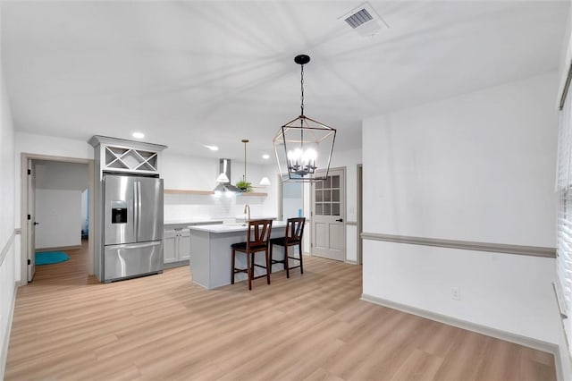 kitchen featuring light countertops, visible vents, a kitchen bar, stainless steel fridge, and light wood-style flooring