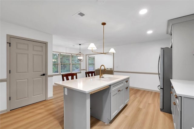 kitchen featuring a sink, light wood-type flooring, freestanding refrigerator, gray cabinetry, and light countertops