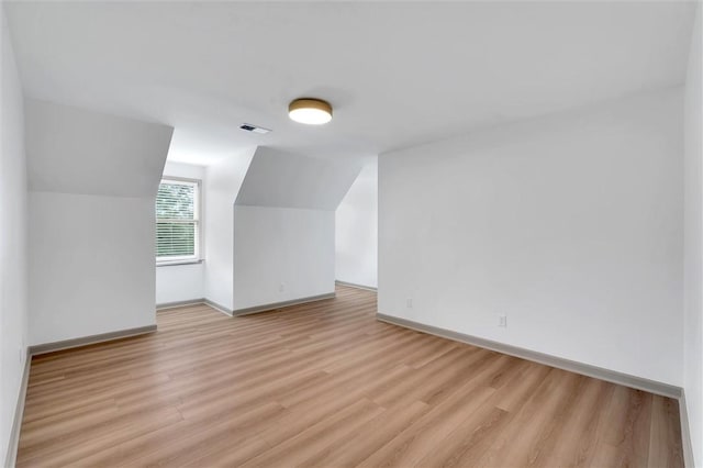 additional living space with light wood-type flooring, baseboards, visible vents, and lofted ceiling