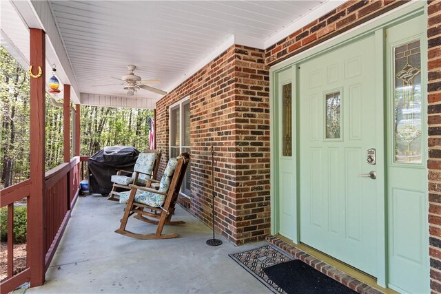property entrance featuring a ceiling fan, covered porch, and brick siding