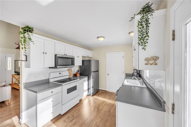 kitchen featuring stainless steel appliances, a sink, dark countertops, light wood-style floors, and white cabinetry