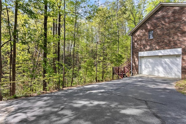 view of home's exterior featuring aphalt driveway, an attached garage, a view of trees, brick siding, and stairs