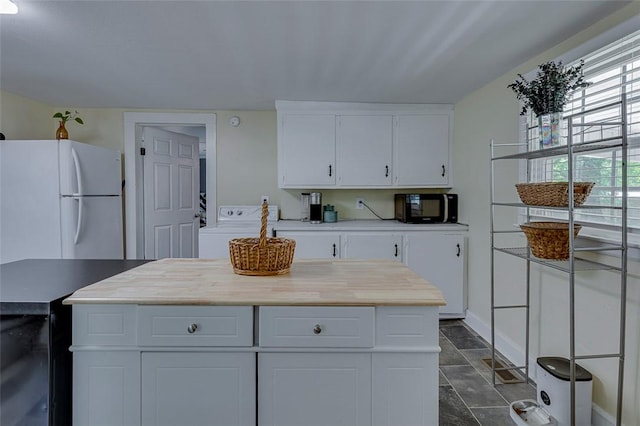kitchen with white cabinets, freestanding refrigerator, black microwave, stone finish flooring, and washer / clothes dryer