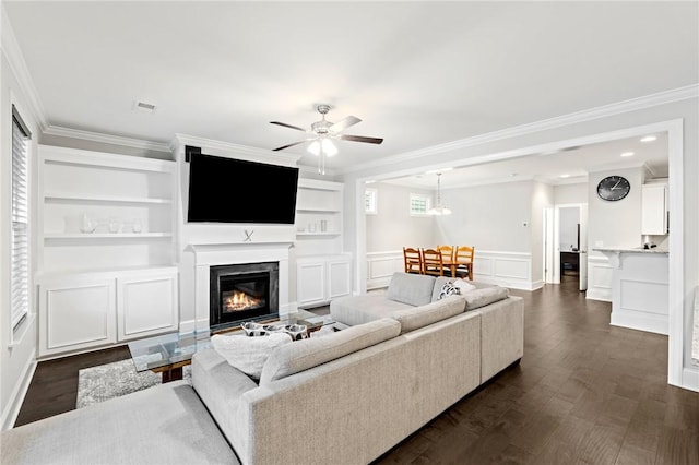 living room featuring a wainscoted wall, crown molding, ceiling fan, a decorative wall, and dark wood-type flooring