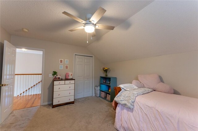 bedroom featuring lofted ceiling, light carpet, a closet, a textured ceiling, and ceiling fan