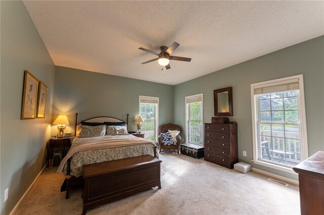 carpeted bedroom with a textured ceiling, visible vents, a ceiling fan, and baseboards