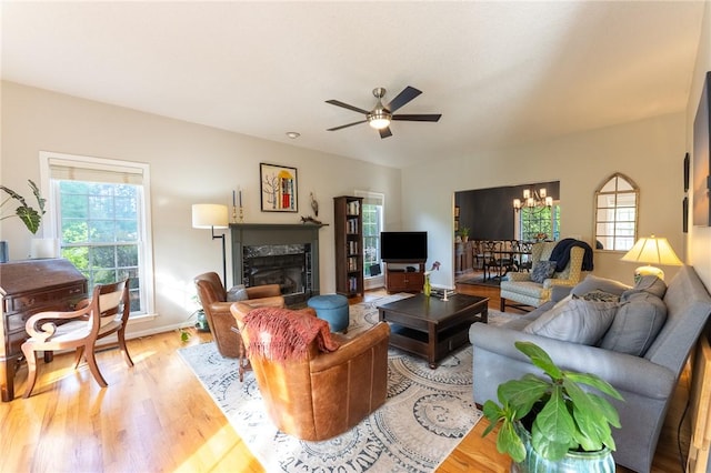 living area featuring baseboards, light wood-style floors, ceiling fan with notable chandelier, and a premium fireplace