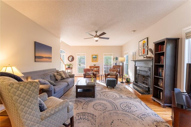 living area featuring a fireplace with flush hearth, wood finished floors, a textured ceiling, and ceiling fan