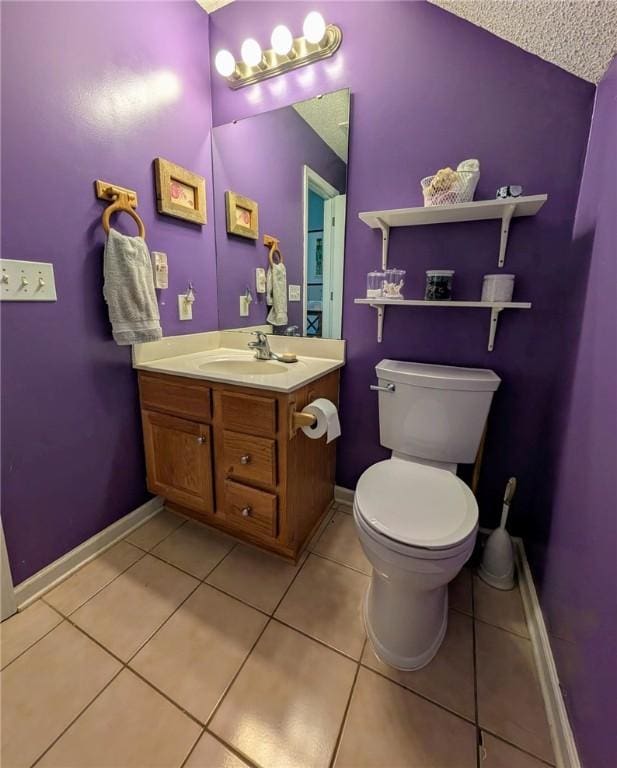 half bathroom with baseboards, tile patterned flooring, vanity, and toilet
