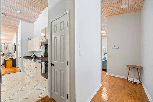 hallway with baseboards, crown molding, wood ceiling, and light wood-type flooring