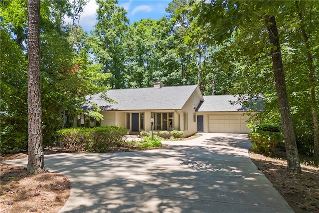 single story home featuring concrete driveway, an attached garage, a chimney, and a shingled roof