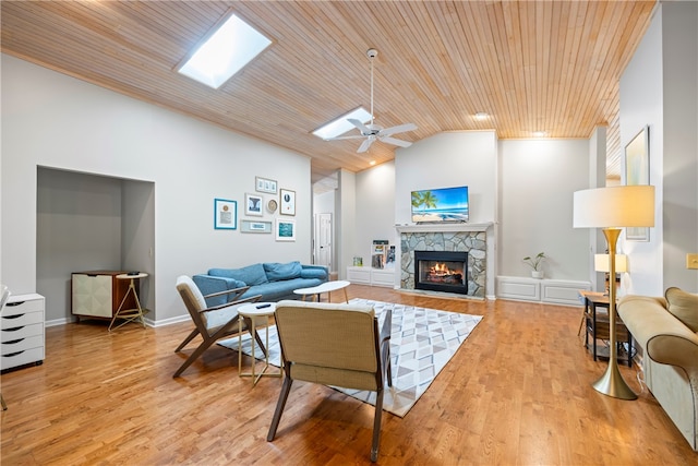 living room with wood ceiling, a stone fireplace, light wood finished floors, and lofted ceiling with skylight