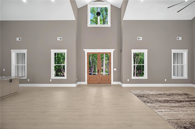 interior space with baseboards, high vaulted ceiling, visible vents, and light wood-type flooring