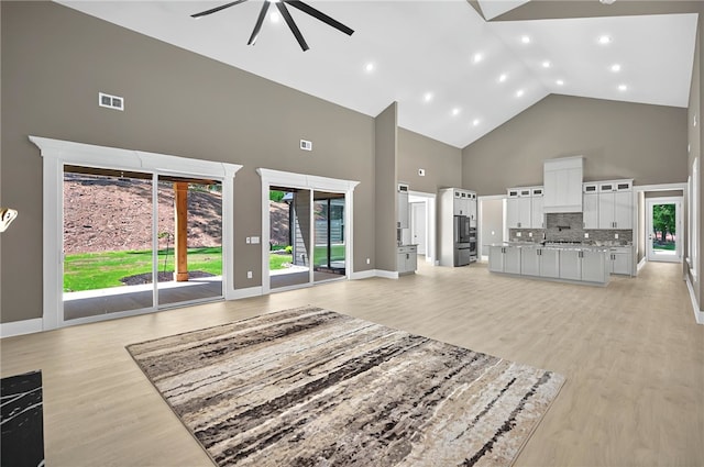unfurnished living room featuring visible vents, a healthy amount of sunlight, light wood-type flooring, a ceiling fan, and high vaulted ceiling