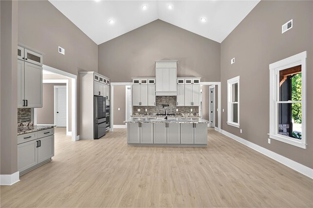 kitchen with visible vents, an island with sink, decorative backsplash, and high vaulted ceiling