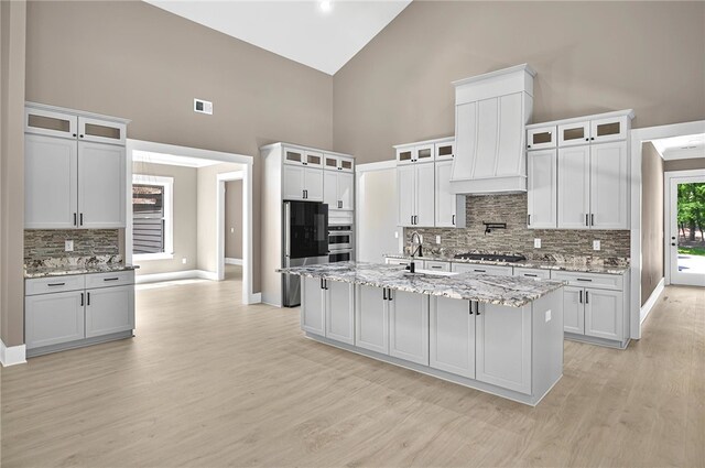 kitchen featuring tasteful backsplash, a sink, appliances with stainless steel finishes, light wood-type flooring, and high vaulted ceiling