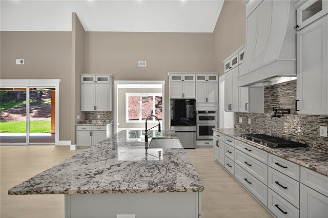kitchen featuring a high ceiling, a sink, decorative backsplash, custom range hood, and appliances with stainless steel finishes