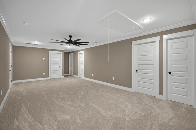 carpeted empty room with attic access, ceiling fan, ornamental molding, and baseboards