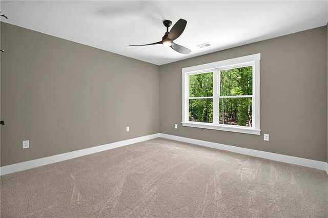 unfurnished room featuring light colored carpet, visible vents, a ceiling fan, and baseboards