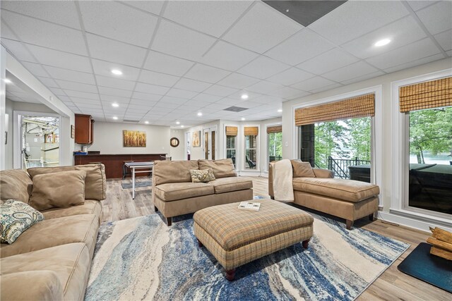 living room with a drop ceiling and light wood-type flooring