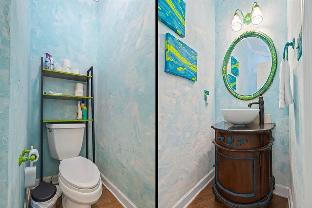 half bath with toilet, wood finished floors, vanity, and baseboards