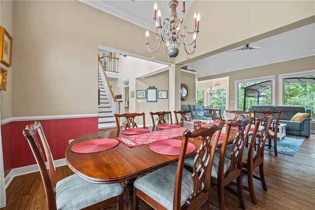 dining space featuring crown molding, stairs, a towering ceiling, wood finished floors, and ceiling fan with notable chandelier