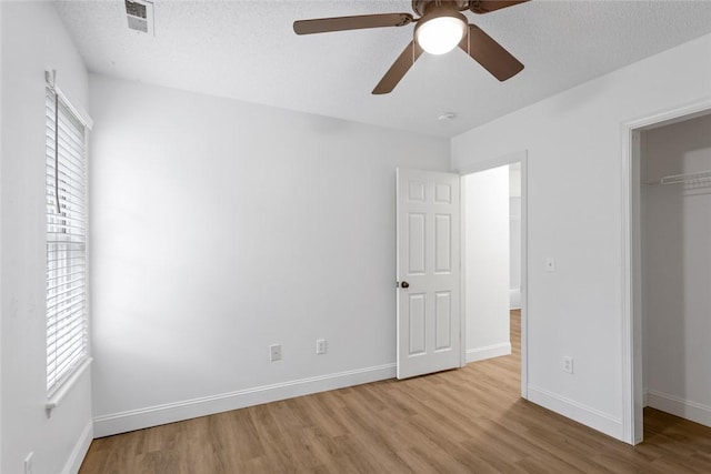 unfurnished bedroom featuring a closet, visible vents, baseboards, a textured ceiling, and wood finished floors