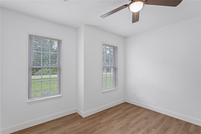 unfurnished room featuring a wealth of natural light, a ceiling fan, light wood finished floors, and baseboards