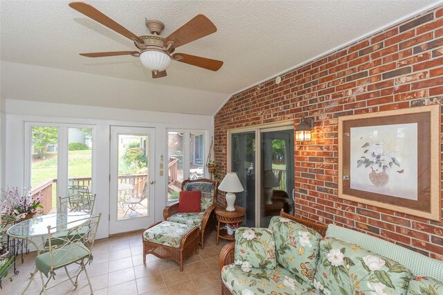 sunroom / solarium with brick wall, tile patterned floors, vaulted ceiling, ceiling fan, and a textured ceiling