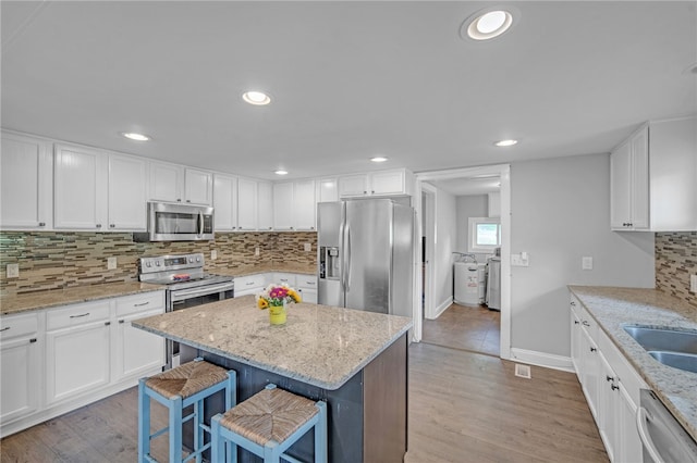 kitchen with white cabinetry, washing machine and dryer, stainless steel appliances, baseboards, and a kitchen bar