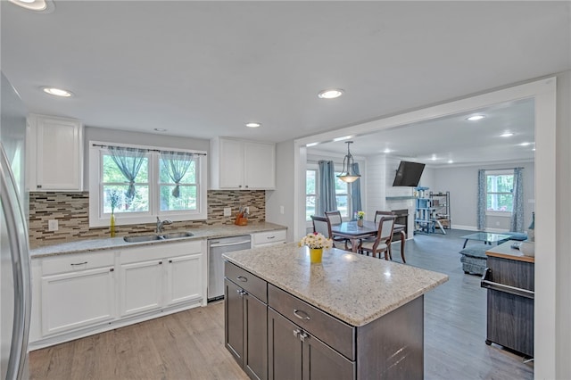 kitchen with white cabinetry, stainless steel dishwasher, light wood-style flooring, a sink, and backsplash