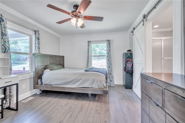 bedroom with ornamental molding, light wood-style flooring, and a barn door