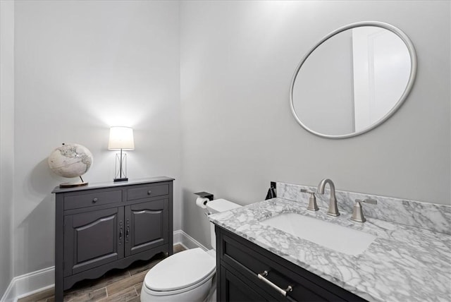 half bathroom featuring baseboards, wood finished floors, toilet, and vanity