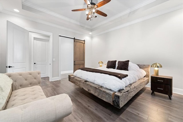 bedroom featuring a barn door, a tray ceiling, wood finished floors, and baseboards