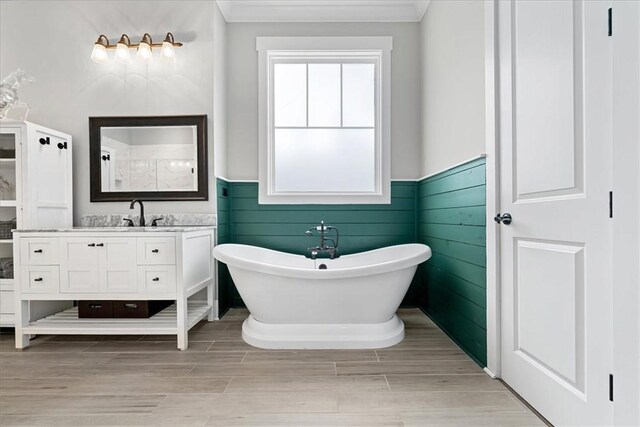 full bath featuring ornamental molding, vanity, a wainscoted wall, and a soaking tub