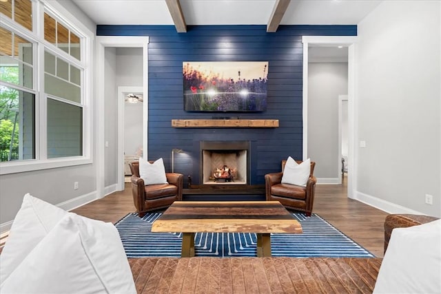 living area featuring beam ceiling, wood finished floors, a large fireplace, and baseboards