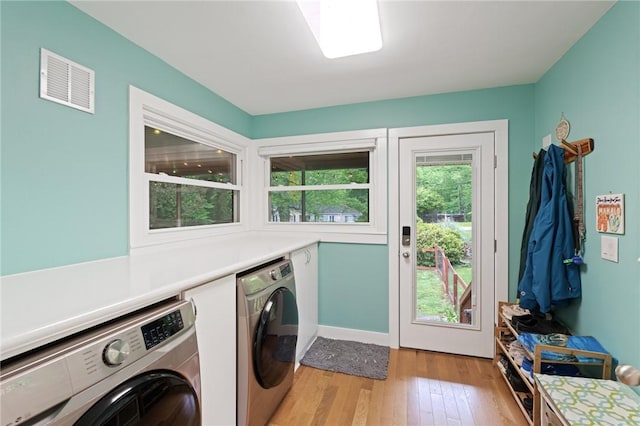 clothes washing area with washing machine and dryer, laundry area, light wood-type flooring, visible vents, and baseboards