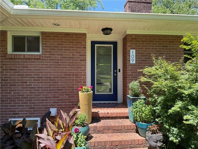 entrance to property with a chimney and brick siding