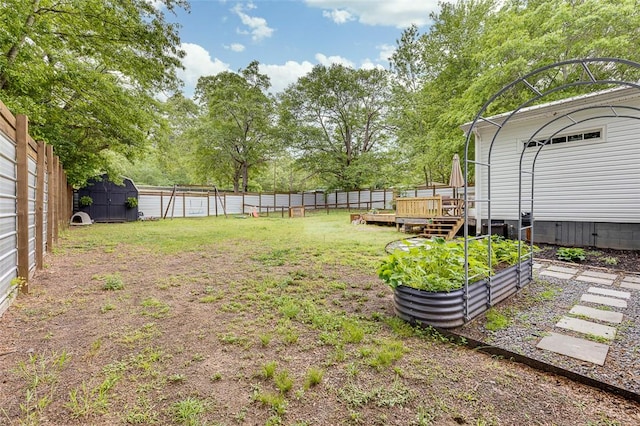 view of yard with an outdoor structure, a vegetable garden, a wooden deck, and a fenced backyard