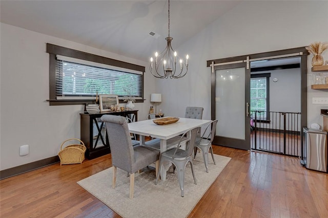 dining area with an inviting chandelier, a barn door, vaulted ceiling, baseboards, and wood finished floors