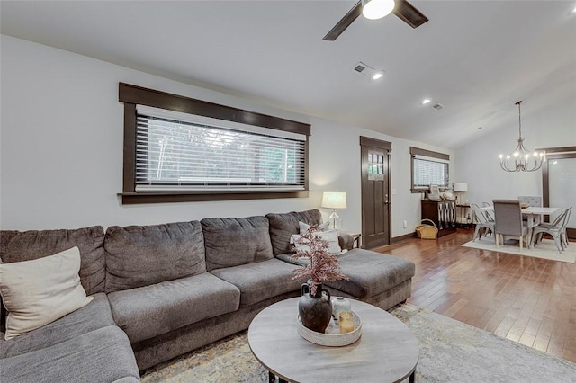 living room with vaulted ceiling, a wealth of natural light, hardwood / wood-style flooring, and ceiling fan with notable chandelier