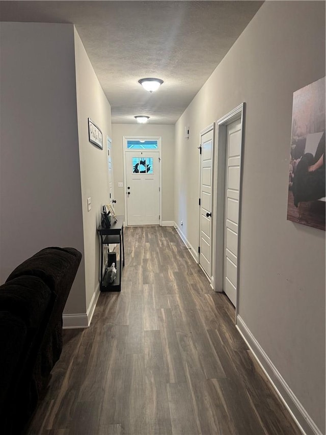 corridor with a textured ceiling, baseboards, and dark wood finished floors
