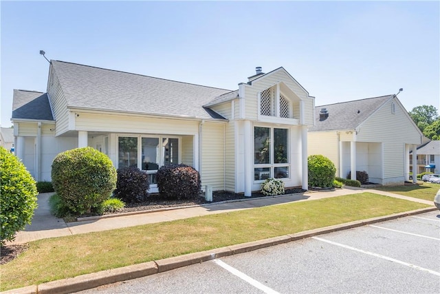 view of front of house featuring a chimney, a front lawn, a shingled roof, and uncovered parking