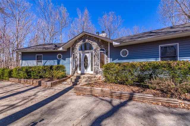 single story home with a chimney and stone siding