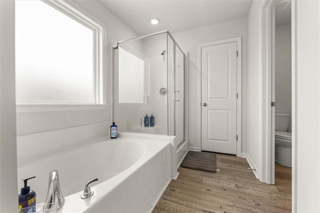 bathroom with toilet, a stall shower, a garden tub, and wood finished floors