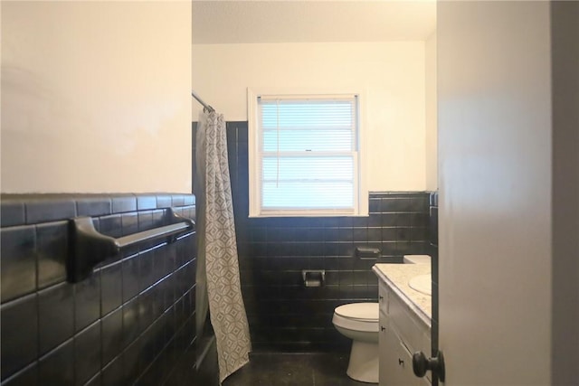 bathroom with wainscoting, tile walls, a shower with shower curtain, toilet, and vanity