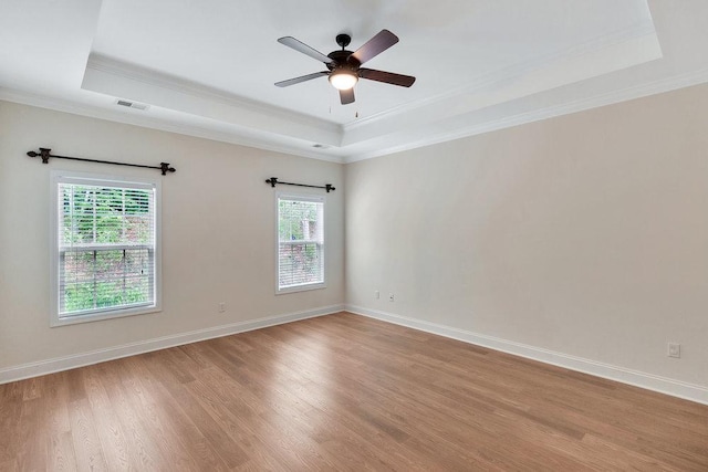 empty room with a ceiling fan, visible vents, crown molding, a tray ceiling, and light wood-style flooring