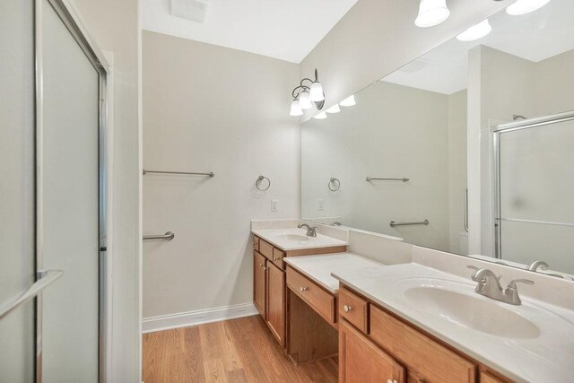 full bathroom featuring a sink, double vanity, a shower with door, and wood finished floors